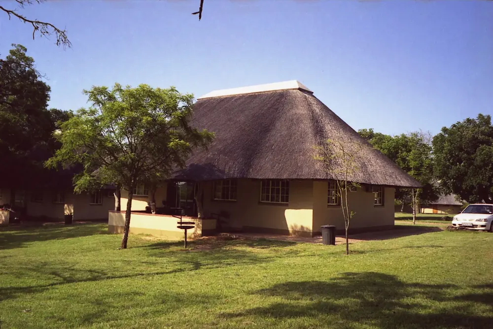 Thatched round house in Pretoriuskop rest camp in Kruger National Park on a lawn between trees