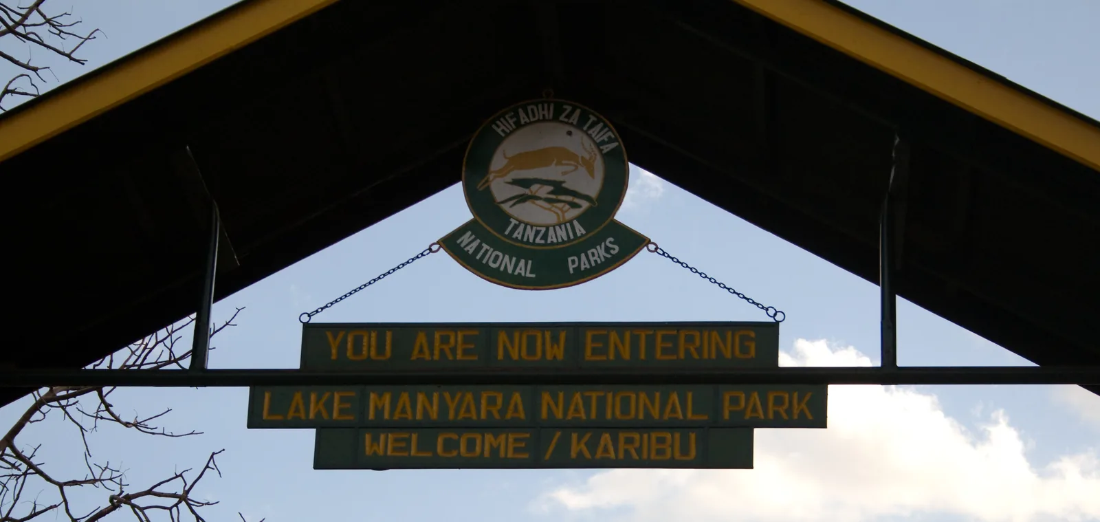 Archway at the main entrance to Lake Manyara National Park with the sign “You are now entering Lake Manyara National Park – Welcome/Karibu” and the park emblem