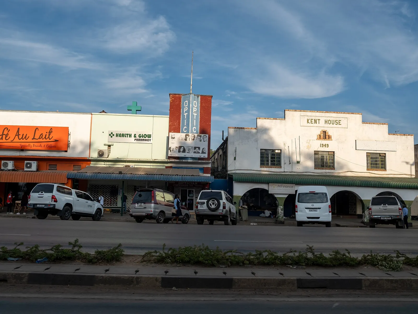 Mosi-oa-Tunya Road in Livingstone with the white Kent House of 1949 and shops, parked cars in front