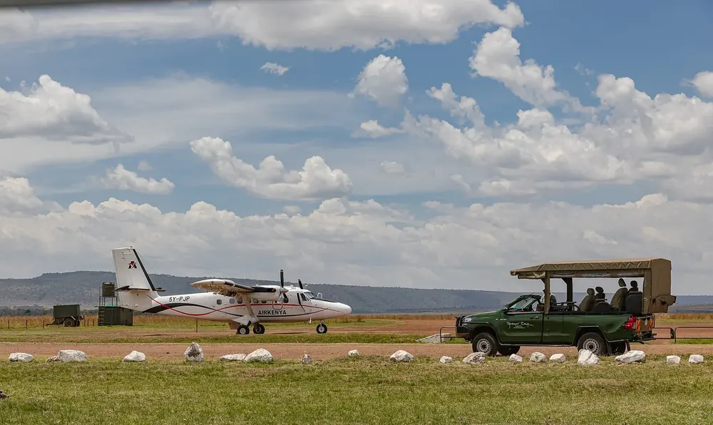 Musiara Airstrip in the Maasai Mara: a small propeller aircraft and a safari vehicle on the grass runway under cumulus clouds