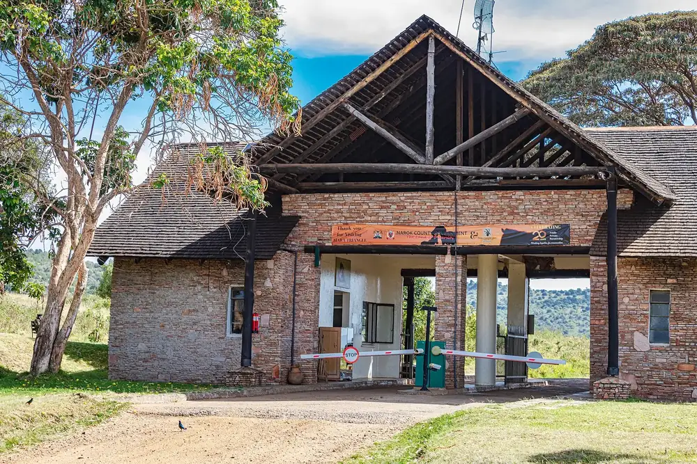 Oloololo Gate of the Maasai Mara: brick gatehouse with a tall wooden gable and a barrier, acacias beside it