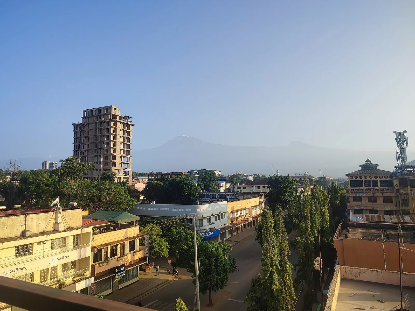 View over the rooftops of Moshi with a tower block, shops and trees, Kilimanjaro on the hazy horizon