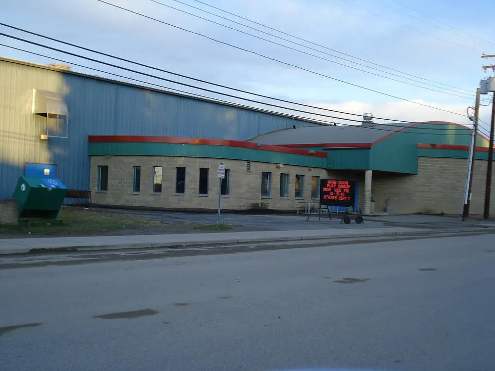 Recreation centre in Fort Simpson: a low building with a red and green roof edge on a wide street