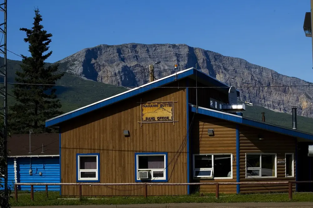Band office in Nahanni Butte: a wooden house with blue trim in front of the steep rock face of Nahanni Butte mountain