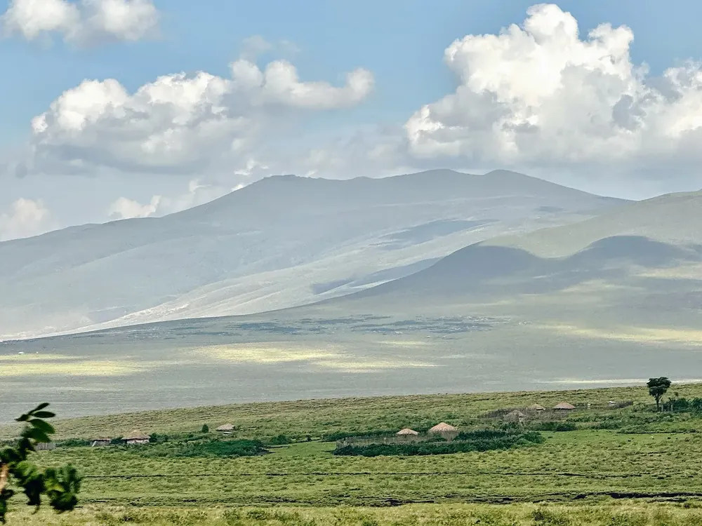 View from Nainokanoka over green highland pastures with Maasai homesteads to Mount Loolmalasin under cumulus clouds