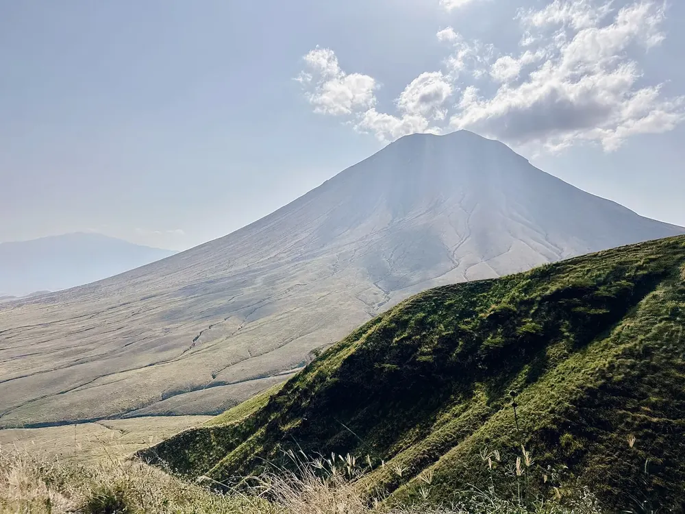 Ol Doinyo Lengai: an evenly shaped grey volcanic cone above the plain, a green ridge in front