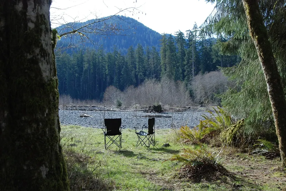 Two camping chairs on a meadow at Hoh Campground in Olympic National Park, with the gravel bed of the Hoh River and forested mountains behind