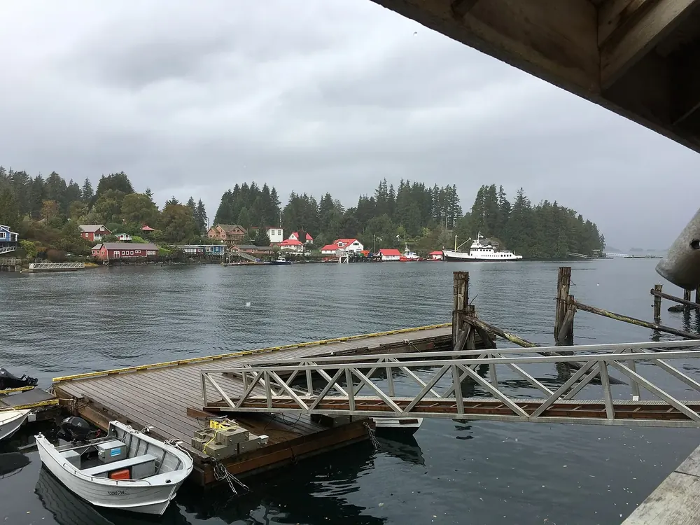 Bamfield harbour: wooden dock with boats in the foreground, houses on the wooded shore of the inlet opposite
