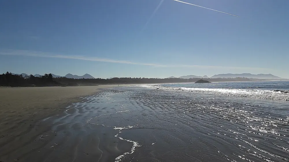 Schooner Cove in Pacific Rim National Park Reserve at low tide: wet sandy beach with glittering channels of water, islands and mountains on the horizon