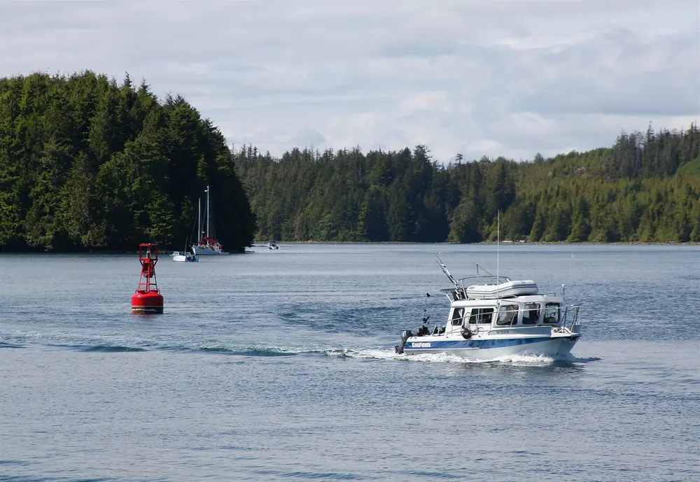 Fishing boat in Ucluelet Inlet, wooded slopes and anchored sailing boats behind