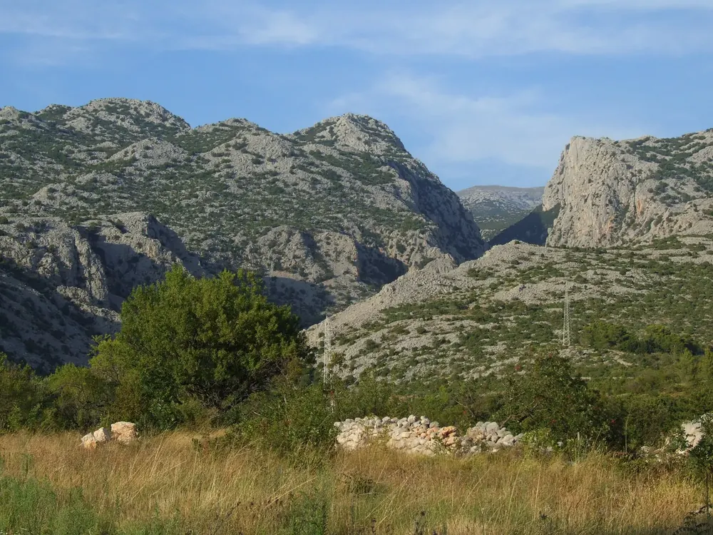 Entrance to Mala Paklenica in Paklenica National Park: barren limestone mountains with a deeply cut canyon, meadow and bushes in front.
