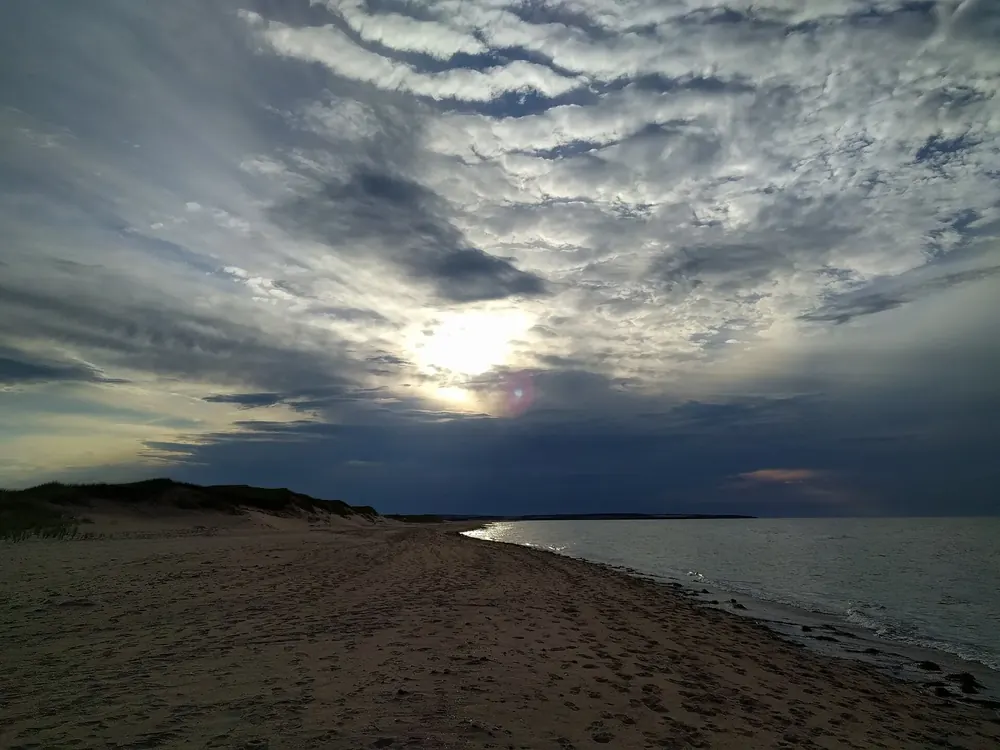 Cavendish Beach in Prince Edward Island National Park at dusk: a long red sand beach with dunes under a dramatic cloudy sky.