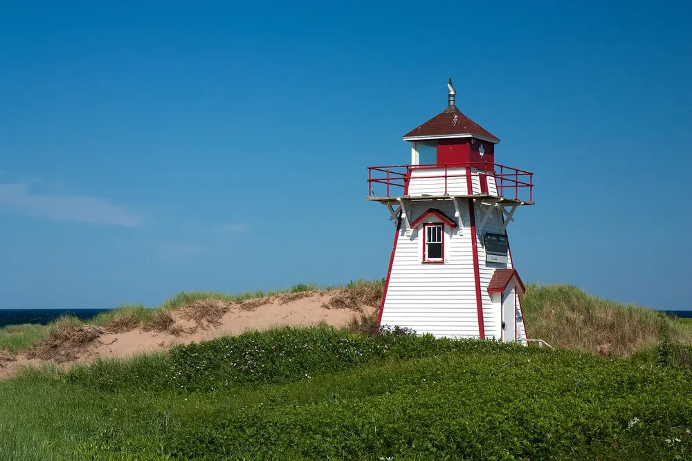 Covehead Lighthouse in Prince Edward Island National Park: white and red wooden lighthouse on a green dune against a deep blue sky.