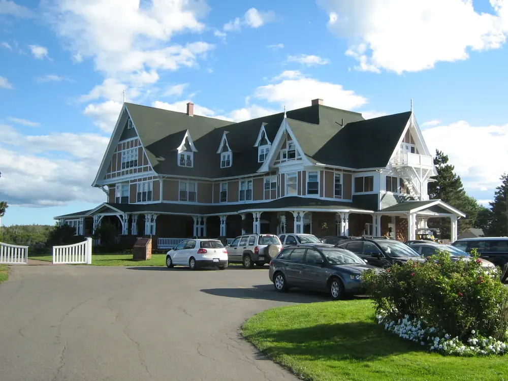 Dalvay-by-the-Sea hotel in Prince Edward Island National Park: historic country house with gables and a wraparound veranda, driveway and lawn in front.