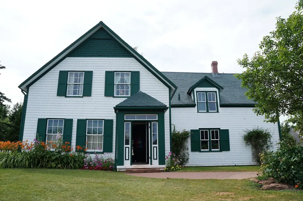 Green Gables House in Cavendish in Prince Edward Island National Park: white wooden house with green shutters and gables, flower beds and lawn in front.