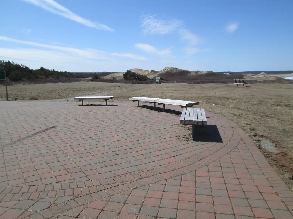 Oceanview Lookout in Prince Edward Island National Park: paved viewing area with wooden benches in front of dunes and grassland in spring.