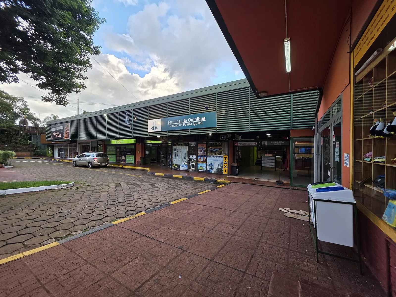 Puerto Iguazú bus station: a long row of shops under a canopy with the sign “Terminal de Omnibus”, a paved forecourt in front