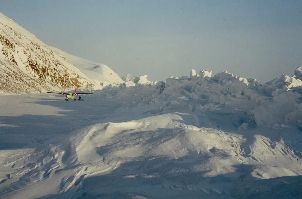 Pressure-ridged sea ice at Cape Columbia in Quttinirpaaq National Park in April, snowy slopes and a small aircraft behind