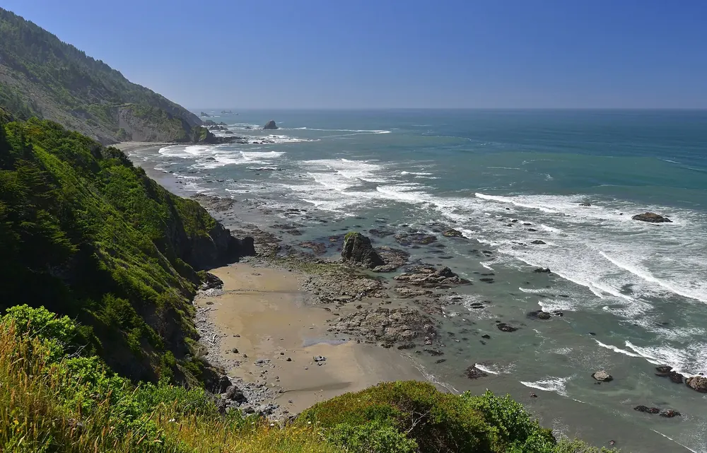 View down from Crescent Beach Overlook in Redwood National Park to Enderts Beach, a rocky surf coast and green steep slopes