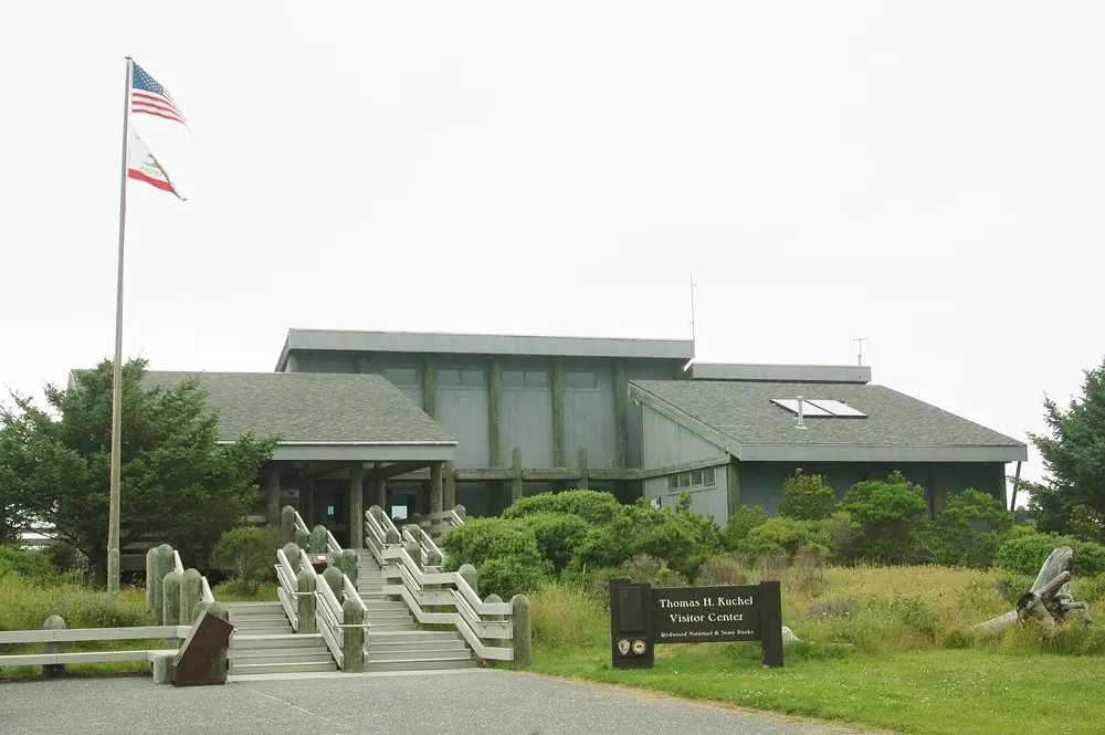 Thomas H. Kuchel Visitor Center: a low wooden building with a flight of steps, a flagpole and coastal vegetation