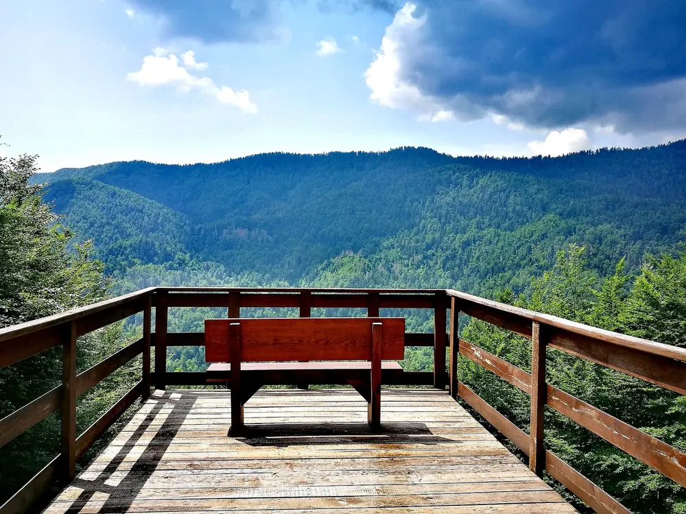 Razloge viewing platform in Risnjak National Park: a wooden bench in front of densely forested mountains under clouds