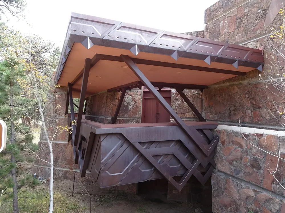Beaver Meadows Visitor Center: cantilevered balcony of rust-red steel on a natural stone facade, with deciduous trees beside it
