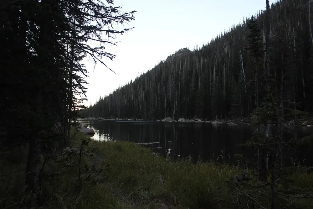 Dream Lake in Rocky Mountain National Park: a long, dark mountain lake between densely forested slopes, backlit