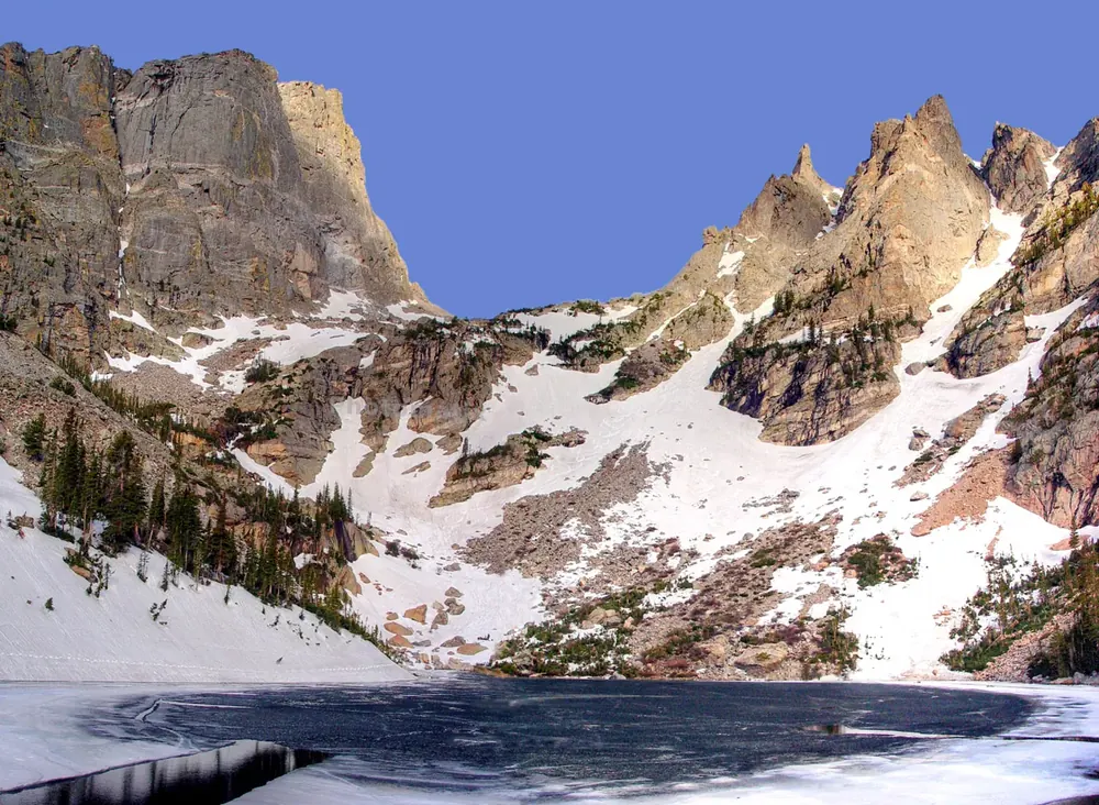 Emerald Lake in Rocky Mountain National Park in spring: a partly frozen mountain lake below steep, partly snow-covered rock walls
