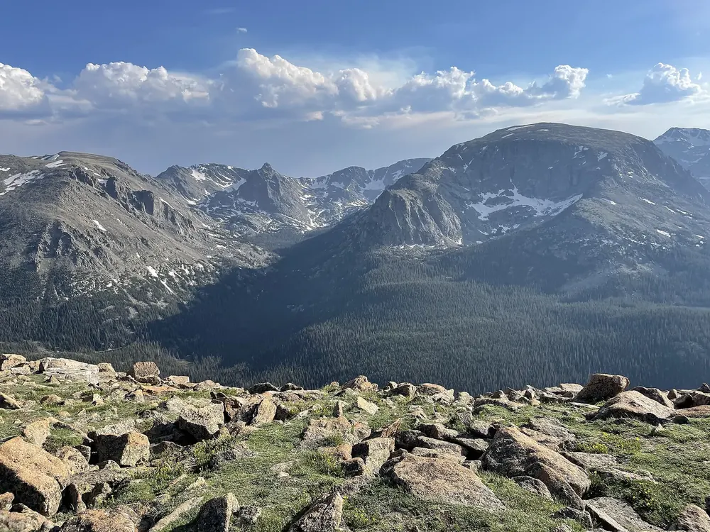 View from Forest Canyon Overlook in Rocky Mountain National Park across boulders and tundra down into the forested Forest Canyon, with peaks behind