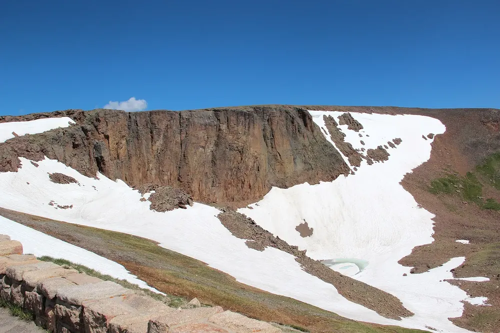 Lava Cliffs in Rocky Mountain National Park: a dark rock wall above a cirque with large snowfields and tundra under a blue sky