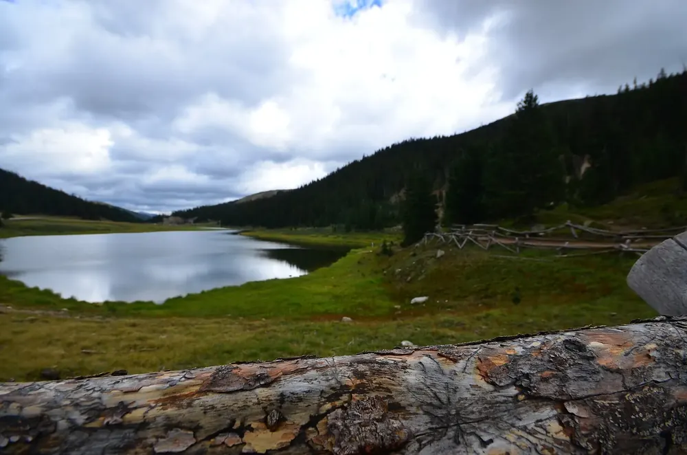 Milner Pass on the Continental Divide in Rocky Mountain National Park: a small mountain lake in the valley between forested slopes under clouds