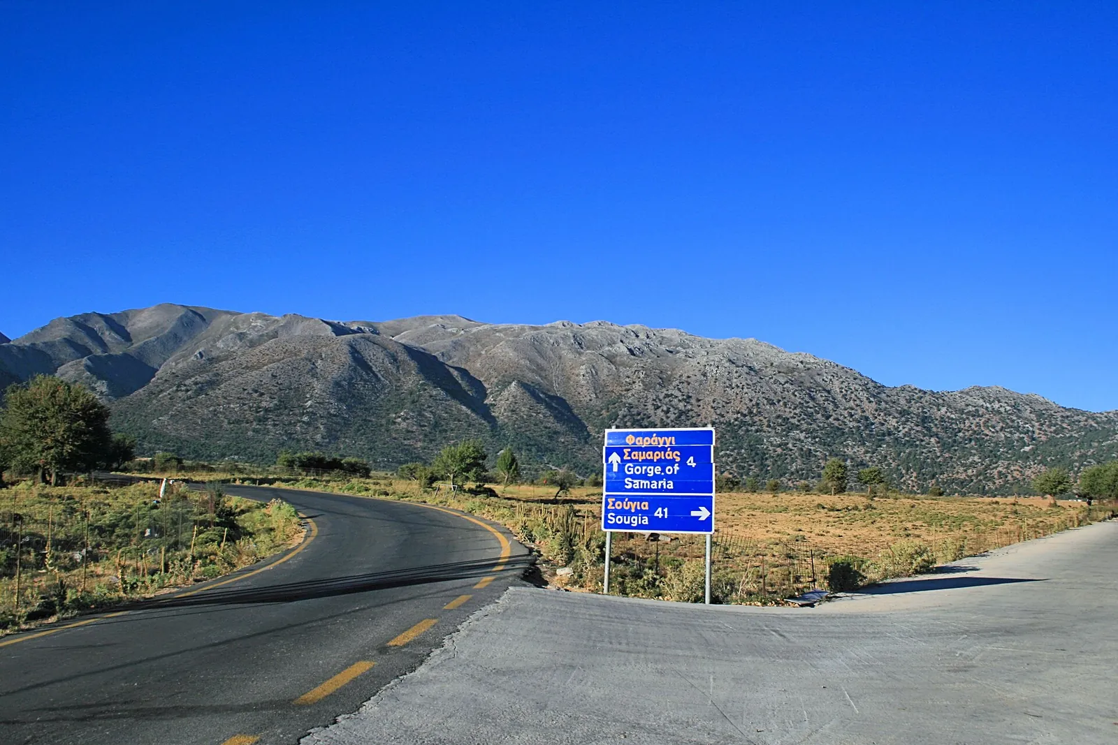 Road across the Omalos plateau with a signpost to the Samaria Gorge, the White Mountains behind