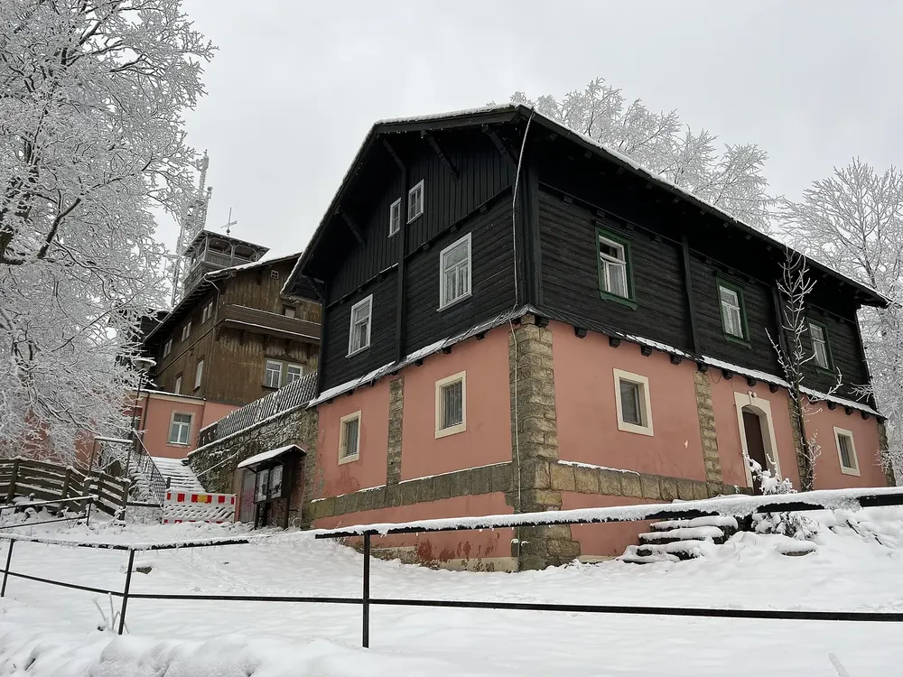 Summit of the Grosser Winterberg in Saxon Switzerland National Park in winter: the former mountain inn with a dark wooden facade between frosted trees