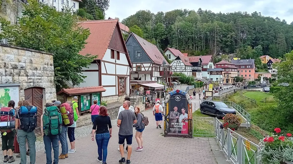 Centre of Kurort Rathen: a lane with half-timbered houses, hikers and a view of the rocks of Saxon Switzerland
