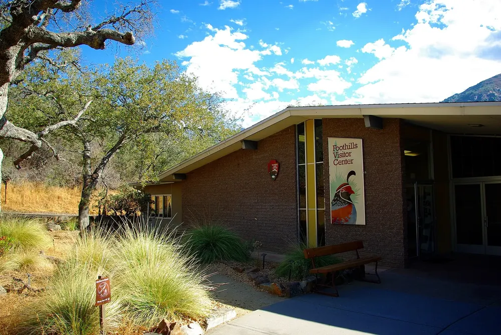 Foothills Visitor Center in Sequoia National Park: low brick building with a canopy and park banner, grasses and oaks in front under a blue sky