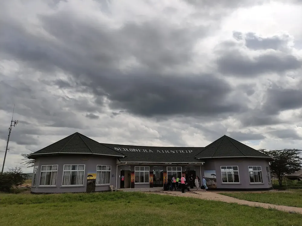 Seronera Airstrip in Serengeti National Park: terminal building with lettering under dark clouds, a lawn in front