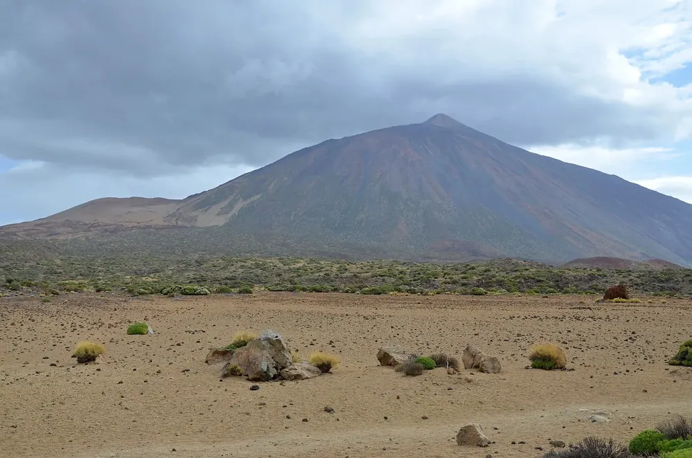 View from La Fortaleza in Teide National Park across the barren plain with broom bushes to Pico del Teide under grey clouds