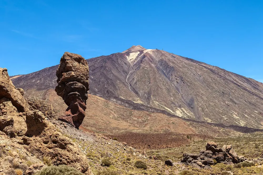 Roque Cinchado in Teide National Park: a narrow, weathered rock tower in front of the massive cone of Pico del Teide under a blue sky