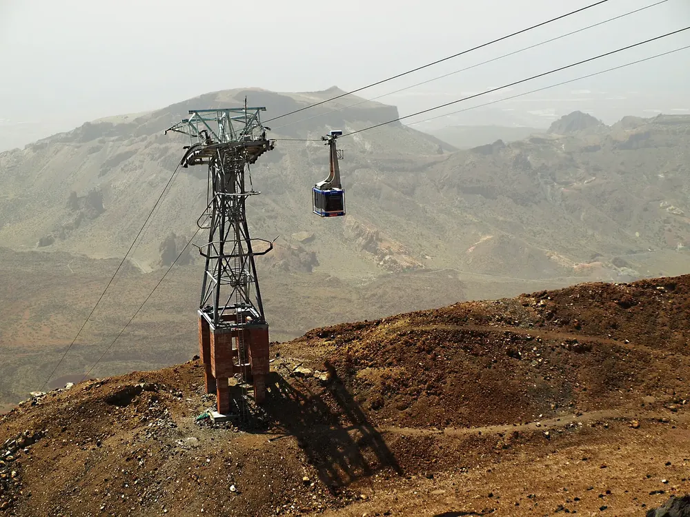 Teide cable car in Teide National Park near the lower station: steel pylon and cabin above the reddish-brown volcanic landscape