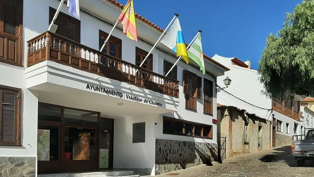 White building with wooden balconies and flags on Calle Francisco Ortuño in Vilaflor