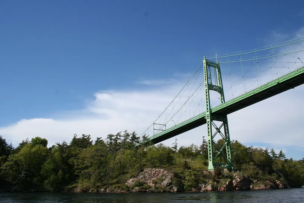 Suspension bridge of the Thousand Islands Bridge over a side channel to forested, rocky Hill Island in Thousand Islands National Park