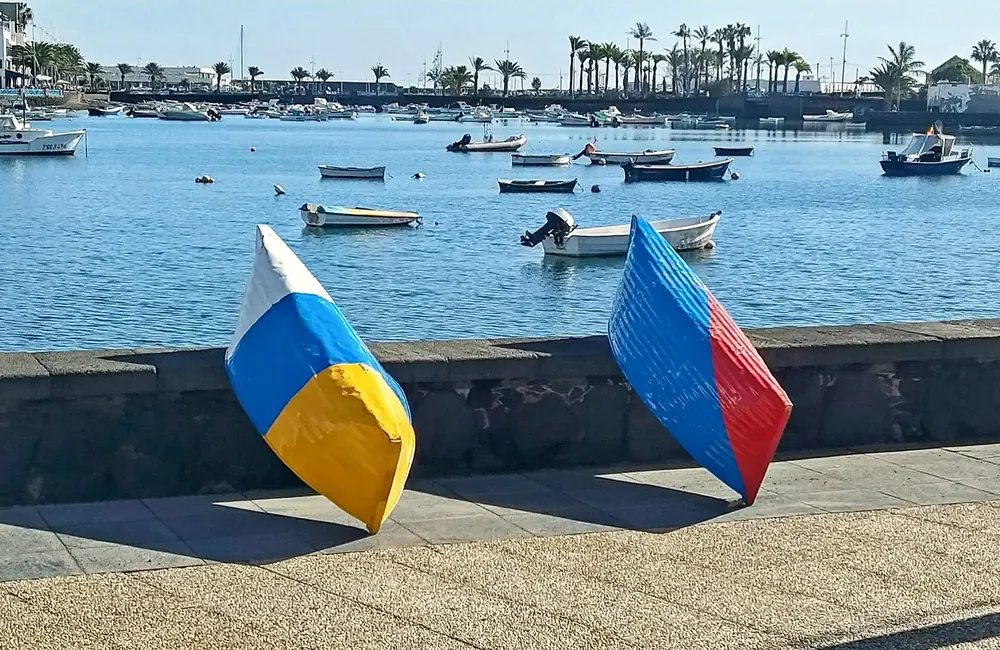 Two brightly painted jolatero boats by the harbour wall in Arrecife, fishing boats in the blue water behind