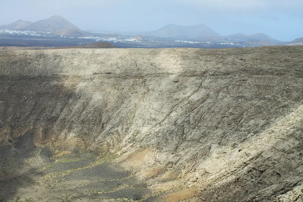 Caldera Blanca: steep, pale inner wall of the tuff ring, with a wide plain and Lanzarote's volcanic cones behind