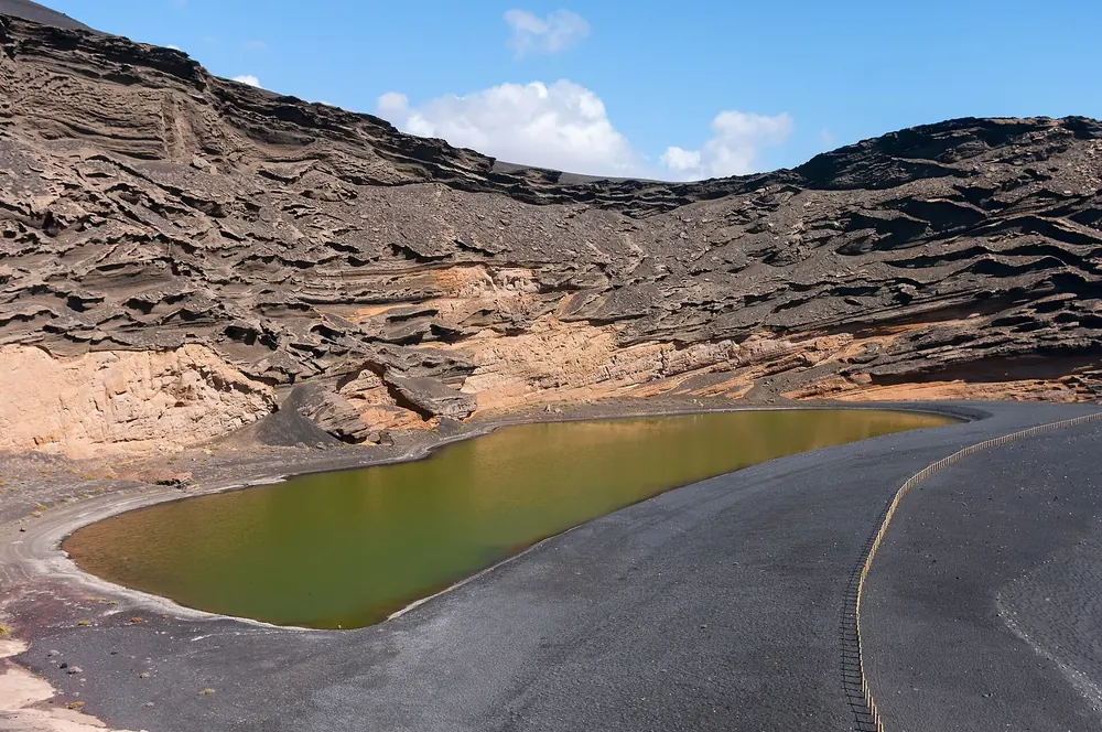 Charco de los Clicos: olive-green lagoon on the black beach below the layered walls of the El Golfo crater