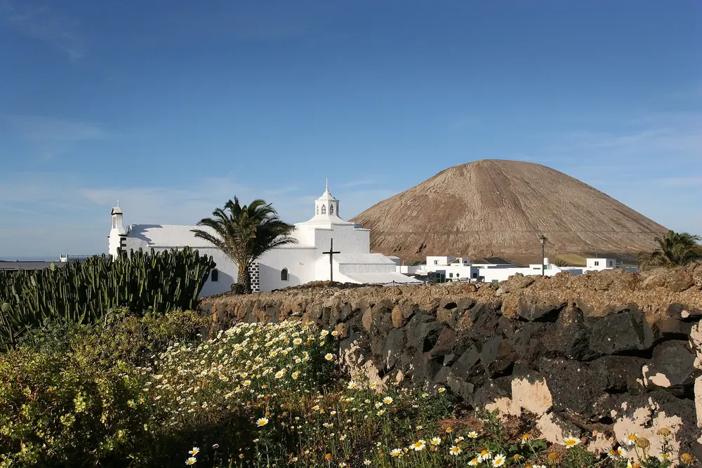 Mancha Blanca: the white church of Nuestra Señora de los Dolores with palm trees in front of a volcanic cone