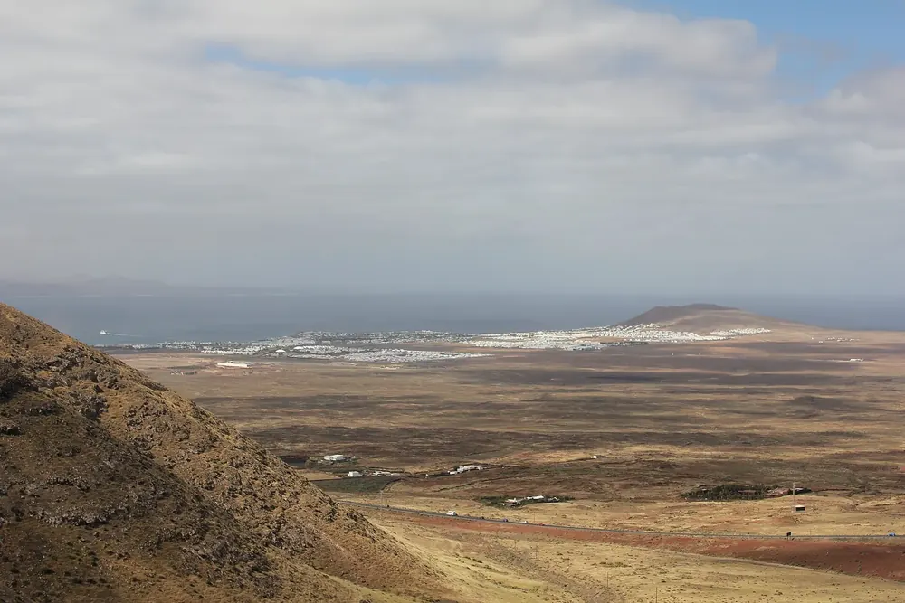 Distant view from the slopes near Femés across the barren plain to Playa Blanca and the sea