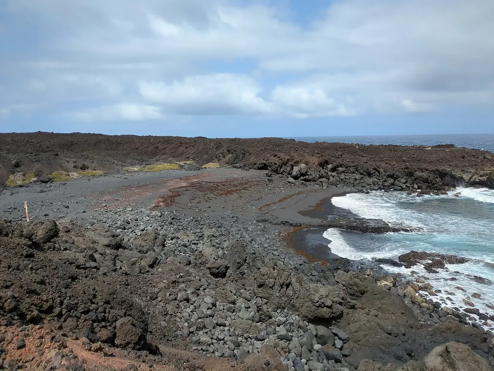 Playa de la Madera: dark lava coast with a small sandy cove and white surf under a cloudy sky