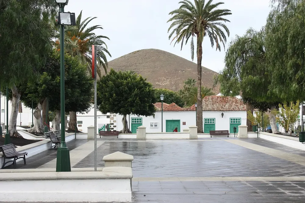 Plaza de los Remedios in Yaiza: a paved square with palm trees and white houses, a volcanic cone behind