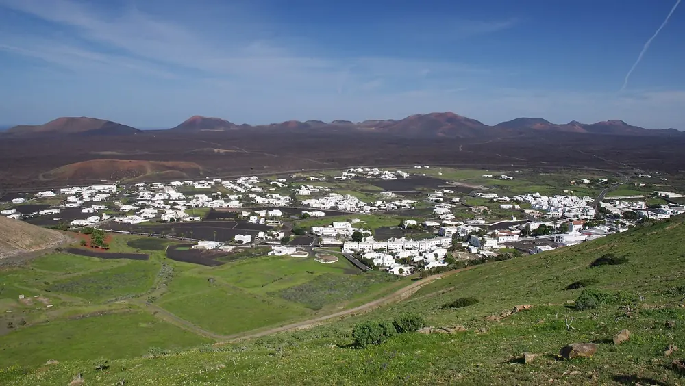 View of Yaiza: white houses among green fields, with the dark volcanic cones of the Fire Mountains behind
