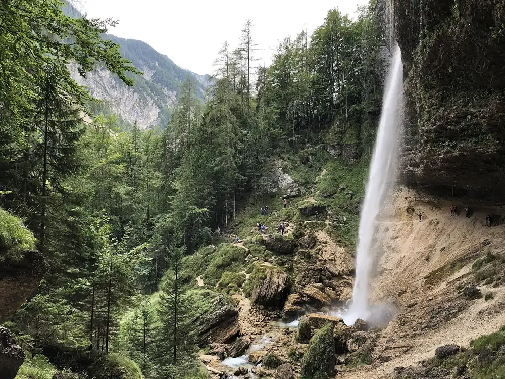 Peričnik Waterfall in Triglav National Park: water plunges over an overhanging rock edge into the forest, with mountain slopes behind